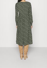Robe florale verte à manches longues avec une taille ajustée et une jupe évasée, associée à des bottes beiges hauteur genou. Tissu texturé avec de petites fleurs blanches.
