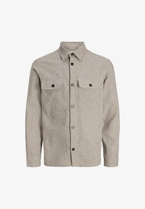 Barn iført beige knap-op tekstureret skjorte, grønne fløjlsbukser og hvide sneakers, stående mod en ensfarvet lys baggrund.