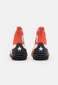 Sneaker high-top in tela arancione con suola in gomma nera, caratterizzate da dettagli a forma di stella bianchi e cuciture a contrasto lungo le cuciture.