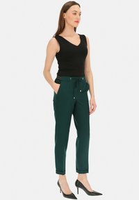 Czarna bezrękawnik połączona z ciemnozielonymi, zwężanymi spodniami z elastycznym paskiem w talii i podwiniętymi nogawkami, uzupełniona czarnymi szpilkami.