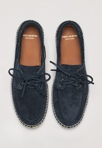 Bateau en suède bleu marine avec un design à lacets, doublure intérieure beige et semelle à couture légère. "FRED MARTIN FABRIQUÉ EN ESPAGNE" est embossé à l'intérieur.