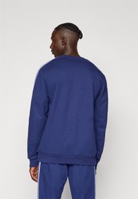 Μπλε ναυτικό φούτερ  με μακριά μανίκια, στρογγυλή λαιμόκοψη και λευκές ρίγες στο πλάι. Απαλή υφή με άνετη εφαρμογή, ορατές ραφές.