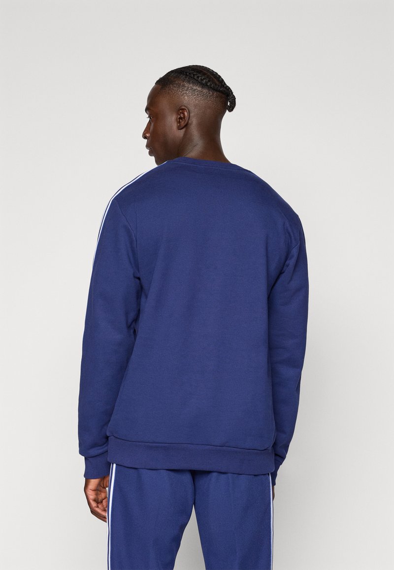 Sudadera azul marino con mangas largas, cuello redondo y franjas laterales blancas, hecha de una tela suave y texturizada.
