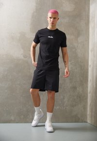 Black t-shirt with logo, black shorts, and white sneakers. Smooth fabric, fitted shape, sitting against a concrete background.