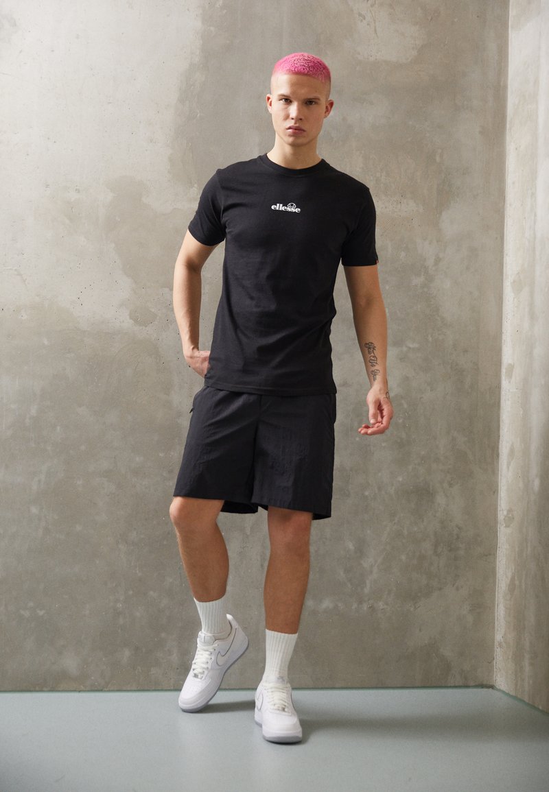 Black t-shirt with logo, black shorts, and white sneakers. Smooth fabric, fitted shape, sitting against a concrete background.
