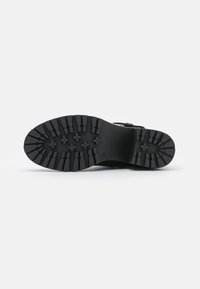 Suela de bota de goma negra con un patrón texturizado, que presenta surcos profundos y un logotipo prominente. Construcción sólida con un diseño resistente.