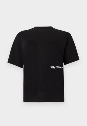 Melnā kokvilnas T-kreklā ar apaļu kakla izgriezumu un īsām piedurknēm, ar baltu tekstu "Karl Lagerfeld Jeans" kreisajā pusē.