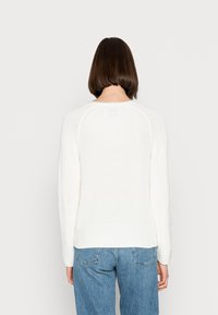 Biały sweter z dzianiny z prążkowanymi akcentami, z okrągłym dekoltem i długimi rękawami. Widok od tyłu ukazuje teksturowany wzór.