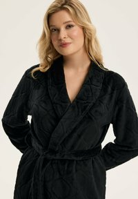 Czarny, teksturowany szlafrok wykonany z miękkiego materiału, z kołnierzem szala, paskiem do związania i wzorzystymi akcentami, idealny do relaksu lub wypoczynku.