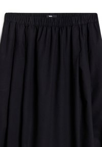 Jupe noire à taille élastique avec étiquette logo Vans centrée en haut, montrant la texture du tissu froncé et une coupe ample.