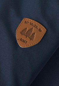 Granatowy materiał z teksturowanym, brązowym skórzanym naszywką w kształcie tarczy, zawierająca wytłoczone w ciemnym brązie drzewa i współrzędne.