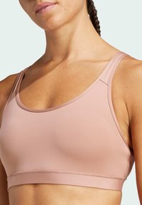 Sujetador deportivo de color rosa claro con una textura suave, tirantes anchos y un escote redondeado. Presenta una costura sutil en el busto y un ajuste que brinda soporte.