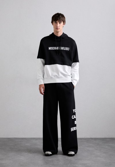 Čierno-biely mikina Moschino s odvážnym textom, spárovaná s širokými čiernymi nohavicami s bielym nápisom. Zmes bavlny, uvoľnený strih.