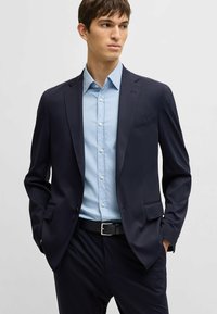 Marineblazer met een slank model, een enkele knoopsluiting, gelapte revers en textuurstof, gecombineerd met een lichtblauwe button-down blouse.