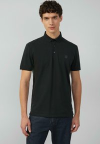 Schwarzes Poloshirt aus Baumwolle, ausgestattet mit einem klassischen Kragen, einer Drei-Knopf-Leiste und einem kleinen Logo auf der Brust. Kurze Ärmel.