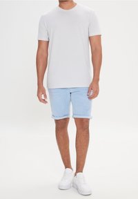 Lichtgrijs t-shirt met korte mouwen en een ronde hals, gecombineerd met lichtblauwe denim shorts met omgeslagen pijpen en witte sneakers.