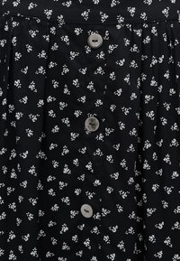 Sort stof med et lille hvidt blomstermønster med en lodret række af fire runde grå knapper.