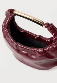 Μπορντώ δερμάτινη τσάντα χεριού με πτυχωτό σχέδιο, χρυσή λαβή και μαύρη υφασμάτινη εσωτερική επένδυση με τσέπη με φερμουάρ.