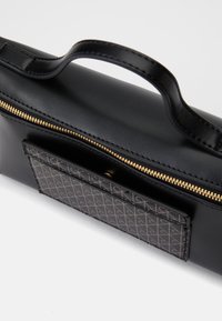 Fekete bőr táska arany cipzárral. Mintás sötét zsebbel, sima textúrával és rövid füllel a tetején a könnyű hordozhatóság érdekében.