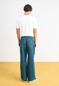 Teal, wide-leg pants made of textured fabric with a straight fit. Features two back pockets and a waistband with elastic.