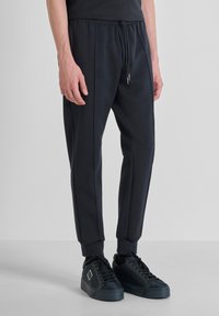 Marineblauwe sweatpants hebben een tapered ontwerp met een elastische tailleband, koordsluiting en zijpiping. Gecombineerd met zwarte sneakers.