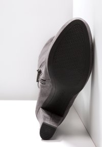 Botín de ante gris con tacón bajo, cremallera lateral y suela de goma que presenta un patrón texturizado. Parte superior lisa y diseño de punta redondeada.