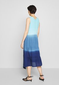 Une robe sans manches à volants avec un effet ombragé allant du bleu clair au bleu foncé, fabriquée dans un tissu léger.