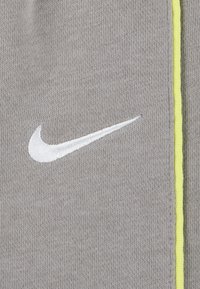 Sivi materijal s mekom teksturom, s bijelim izvezenim Nike logotipom i svijetlo žutom naglaskom duž ruba.