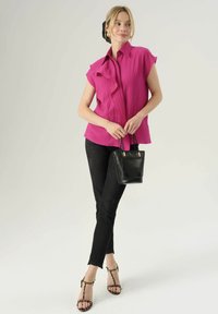 Blusa fucsia a maniche corte con dettagli a volant, abbinata a jeans skinny neri e sandali con tacco. Una borsa nera completa l'outfit.