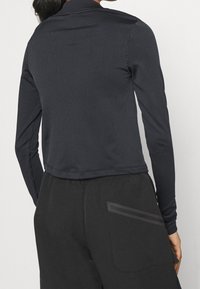 Svart långärmad topp med ribbad textur, hög krage och kort design, kombinerad med mörka byxor med en ficka med dragkedja.