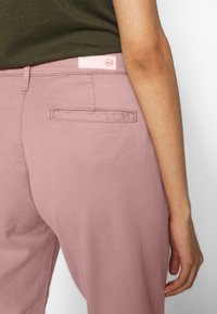 Ljust rosa byxor med en mjuk textur, med en bakficka och en rosa etikett vid midjan. Avslappnad, åtsittande design.