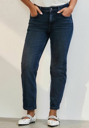 Mörkblå högmidjade jeans med rak benmodell, som har fem fickor och minimala sömnadsdetaljer. Bärs med vita ballerinas med prickar.