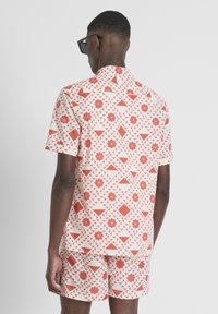 Korte mouwen overhemd en short set in het wit met rode geometrische patronen. Zachte stof, casual vorm, met een kraag en knoopdetails.