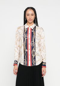 Košulja dugih rukava na kopčanje u krem boji s uzorkom zlatnog lanca, sadrži tamnoplave i crvene okomite pruge te kontrastne manžete.