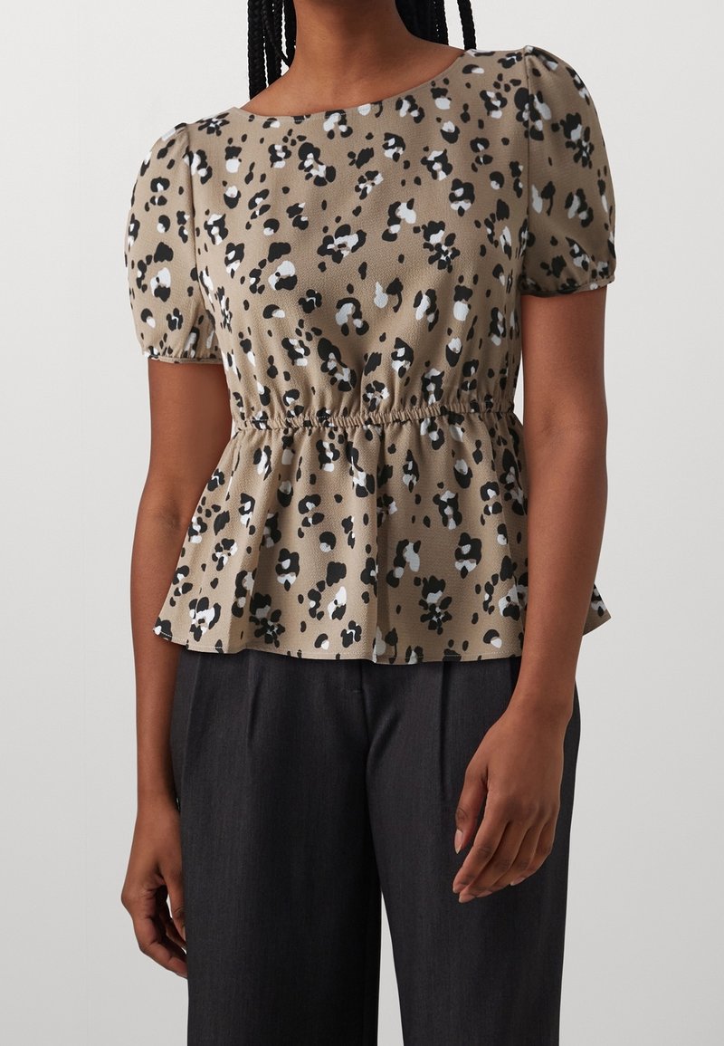 Blusa beige a maniche corte da donna con macchie astratte in bianco e nero, vita arricciata, abbinata a pantaloni ampi grigio scuro.