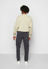 Jeans de denim gris con un logo en el bolsillo trasero, combinados con un sudadera oversized beige. El calzado son zapatillas blancas.