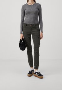 Haut à manches longues gris à côtes, pantalon cargo olive avec poignets élastiques, sac à main en fausse fourrure noir et baskets noires avec rayures blanches et semelle en caoutchouc.