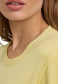 Lichtgele korte mouwen gebreide top met een ronde halslijn en een gladde textuur, voorzien van subtiele stiksels langs de schoudernaden.