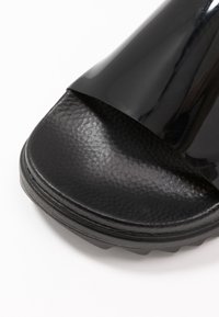 Sort skydesandal med en blank overdel og en tekstureret sort sål. Designet er minimalistisk uden yderligere mønstre eller dekorationer.