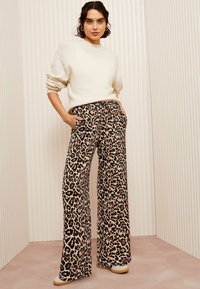 Leopardprint wijde broek met een zwart en tan patroon, gemaakt van zacht materiaal, gecombineerd met een crèmekleurige trui. Platte schoenen maken de look af.