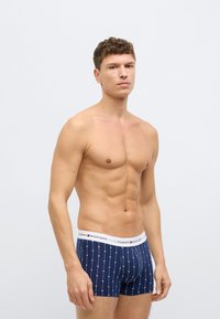 Marineblaue Boxer-Shorts mit weißem elastischem Bund, der ein Logo, ein gepunktetes Muster und ein körpernahes Design zeigt. Baumwollmaterial mit leichter Dehnbarkeit.