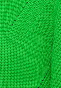 Pull vert tricoté avec un motif texturé ; présente un tissage lâche et des détails en côtes diagonales, mettant en valeur la couleur vive.