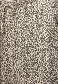 Tissu à motif léopard avec un fond beige clair et des taches gris foncé. Le matériau semble doux avec une légère brillance et un drapé délicat.