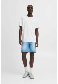 T-shirt en coton blanc, shorts en denim bleu clair, baskets grises et chaussettes blanches. Design simple avec une coupe décontractée.