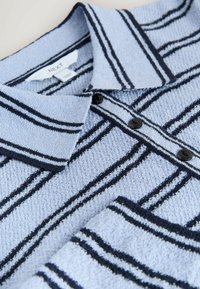 Svetlomodré polo tričko s tmavomodrými pruhmi, textúrovaná látka, tri čierne gombíky na golieri a značková etiketa viditeľná vo vnútri.