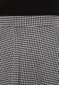 Musta resorivyö, jossa on ruudullinen mustavalkoinen ruutukuvio, teksturoitu kangas vaihtelevalla ruudukkomuodolla.