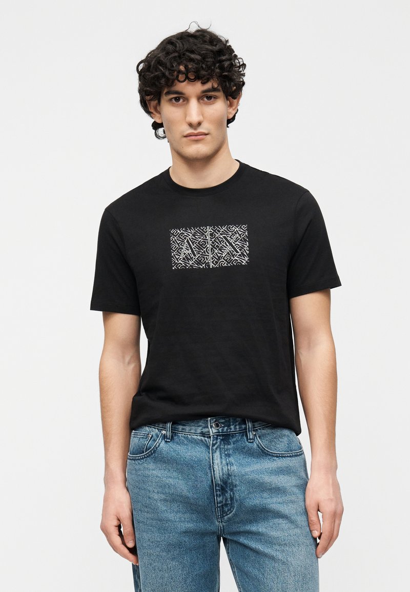 Čierne bavlnené tričko s geometrickým bielym grafickým motívom uprostred na hrudi. Krátke rukávy, okrúhly výstrih a mäkká textúra.