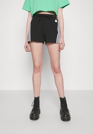 Pantalones cortos negros con rayas blancas, cinturilla elástica y cordón. Combinados con botas negras de cordones. Top verde corto.