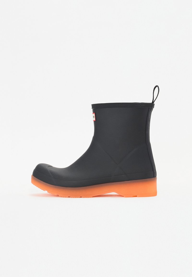 Cizme de ploaie din cauciuc negre, cu talpa portocalie, design până la glezna, finisaj texturat și bucată de prindere în spate. Fără marcaje de brand vizibile.