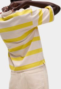 Pruhované tričko s krátkým rukávem z bavlny v krémové a žluté barvě. Obsahuje kulatý výstřih a boční rozparky na lemu. Jemná textura, uvolněný střih.